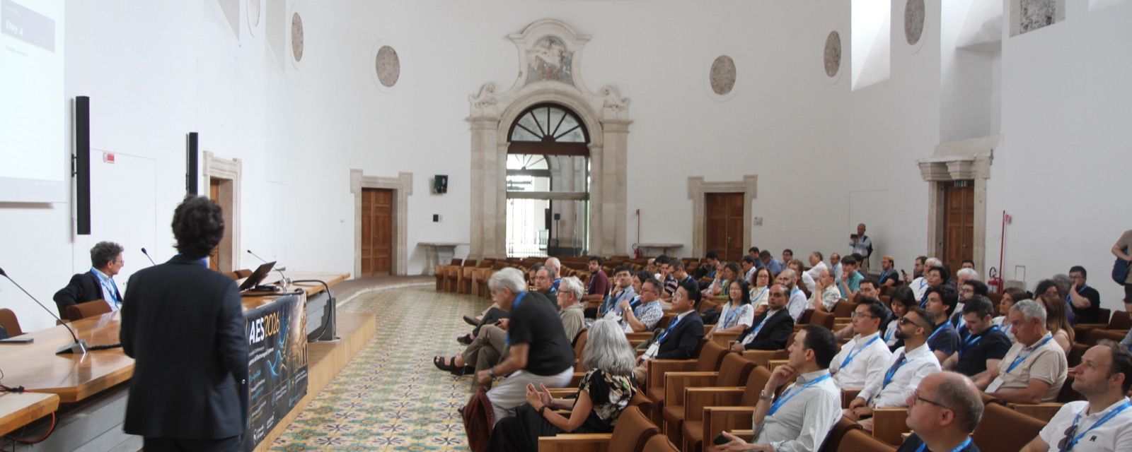 A plenary speaker addressing participants in the main lecture hall at AES 2026 in Catania.