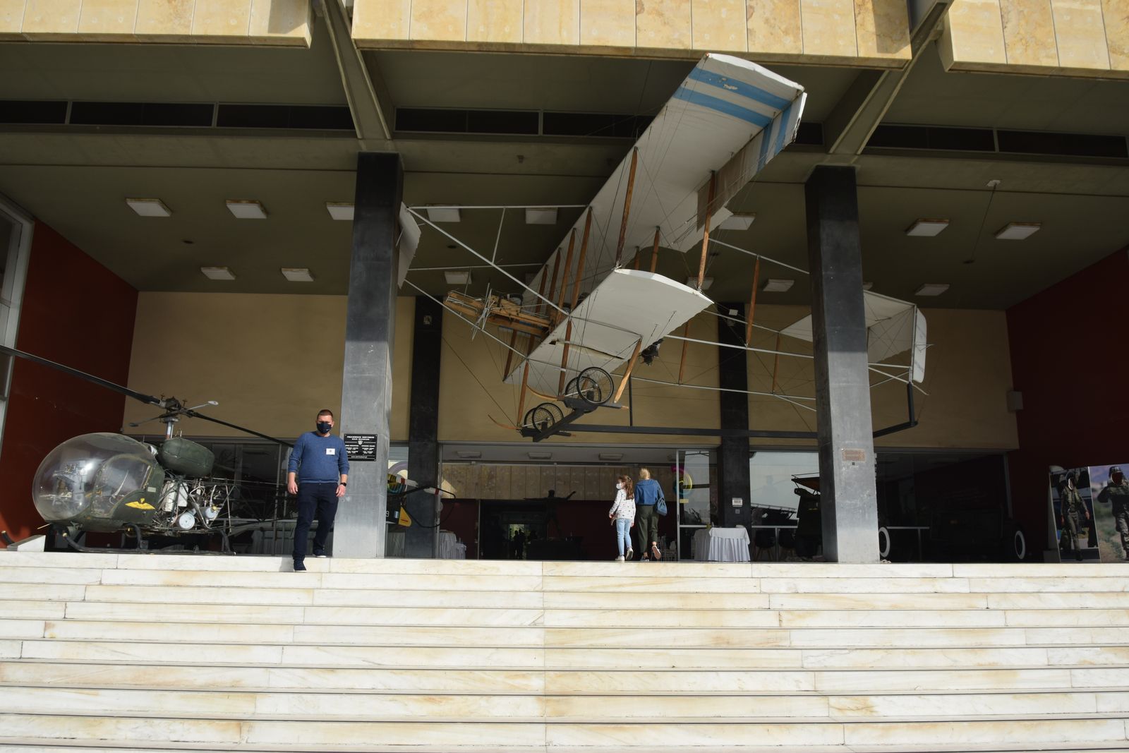 The covered entrance portico of the War Museum of Athens, with a Wright-type biplane suspended between its concrete piers and the steps to Vasilissis Sofias Avenue below